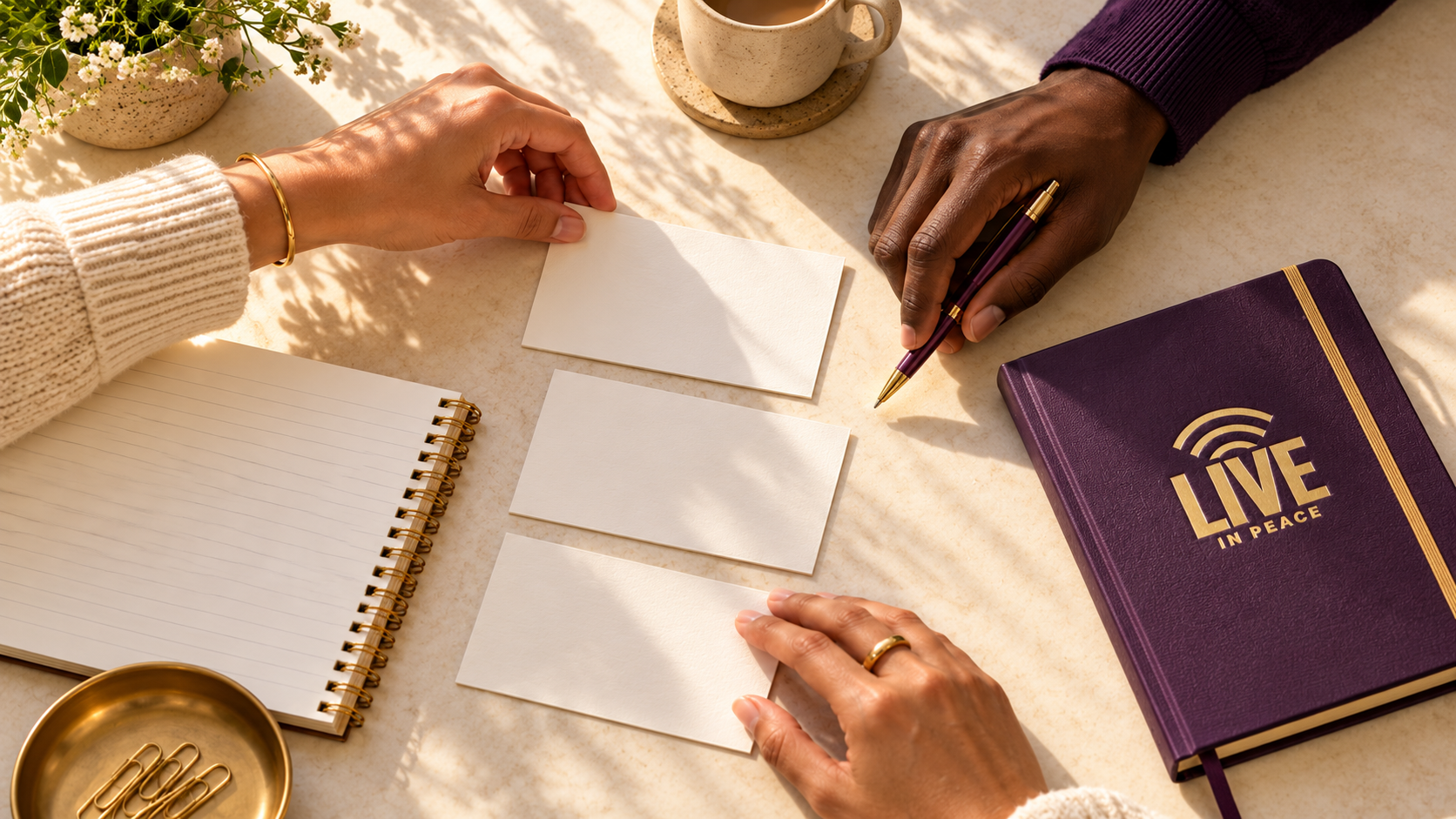 Hands organizing note cards beside a purple notebook with the gold Live In Peace logo